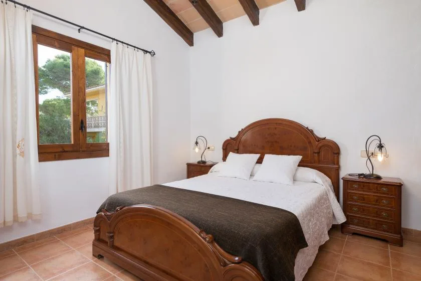 A bedroom with a wooden bed, white bedding, and a window with curtains.