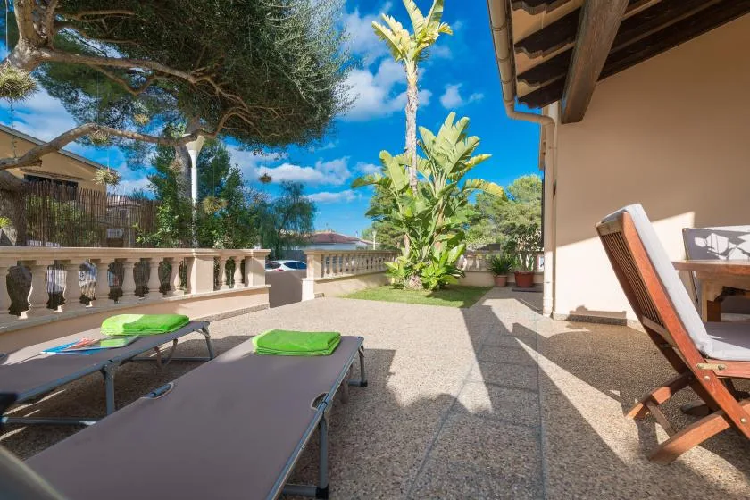 A sunny outdoor patio with reclining loungers and tropical plants.