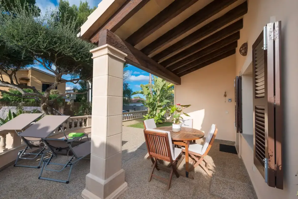 A covered outdoor patio has a dining table and seating beside an open terrace.