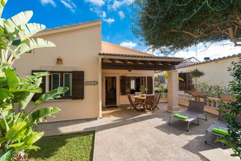 A sunny patio beside a house, with outdoor seating beneath a covered terrace.