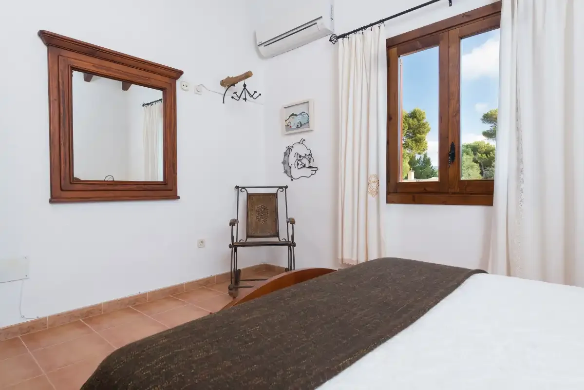 A bedroom with a bed, a wooden-framed window, and a chair.