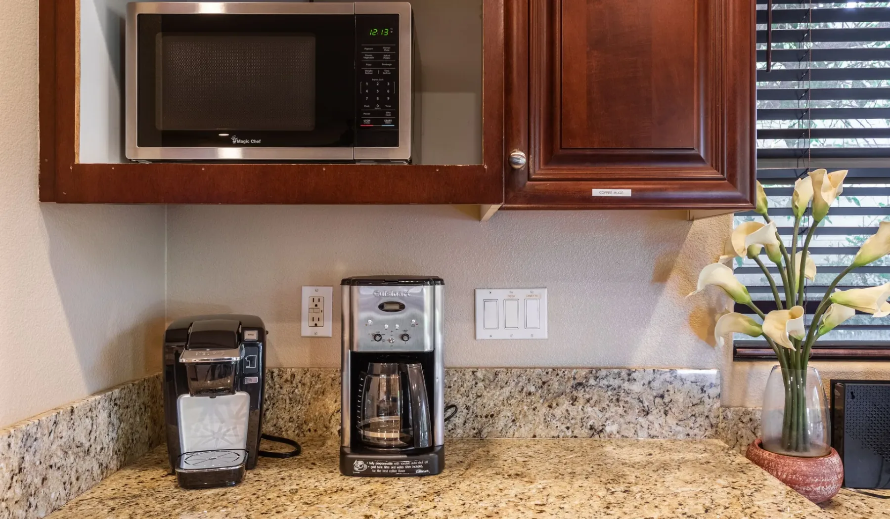 A kitchen counter with coffee makers beneath wooden cabinets and a microwave.