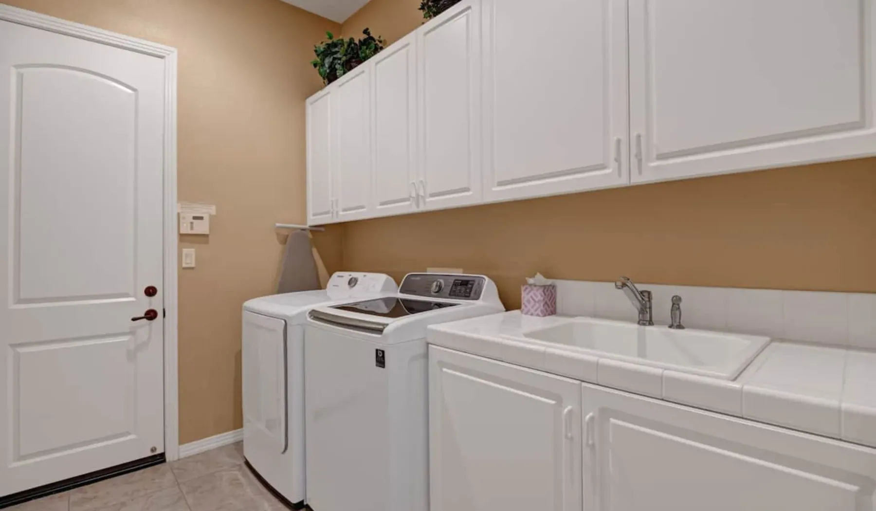 A laundry room with a washer, dryer, and sink beneath white cabinets.