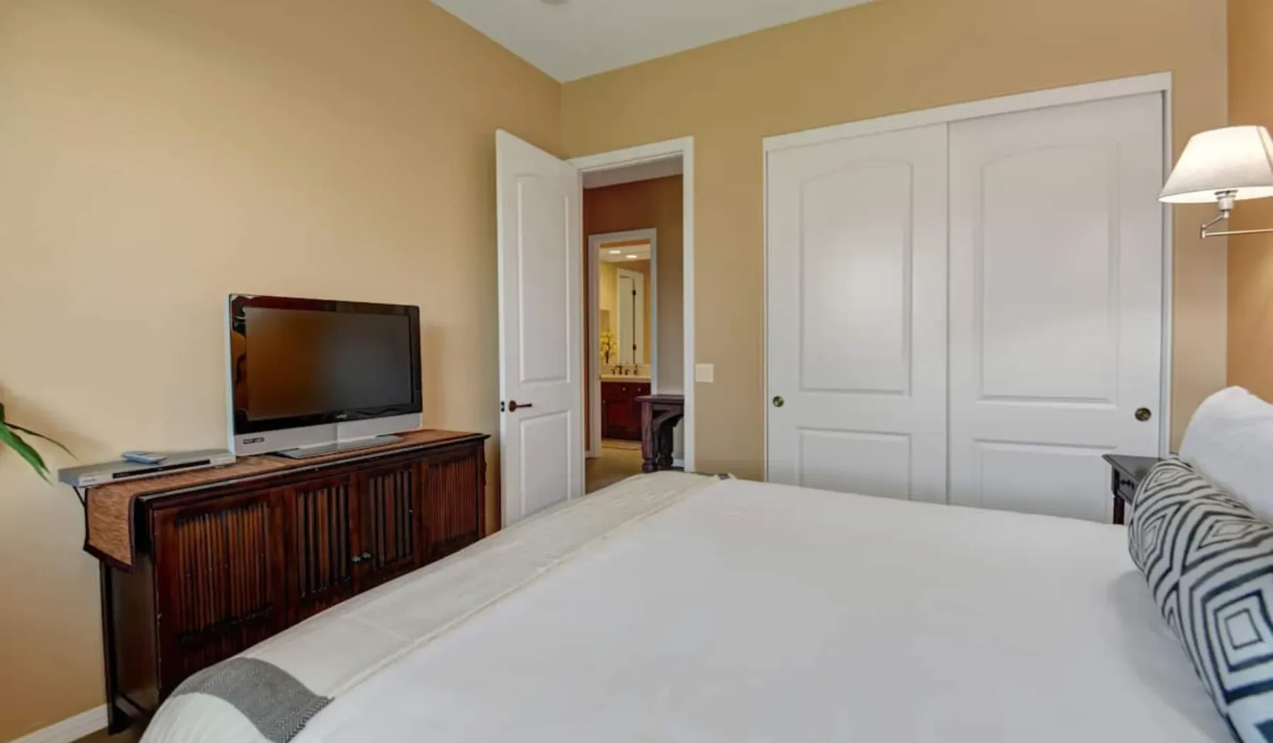 A bedroom with a neatly made bed, television, and closed closet doors.