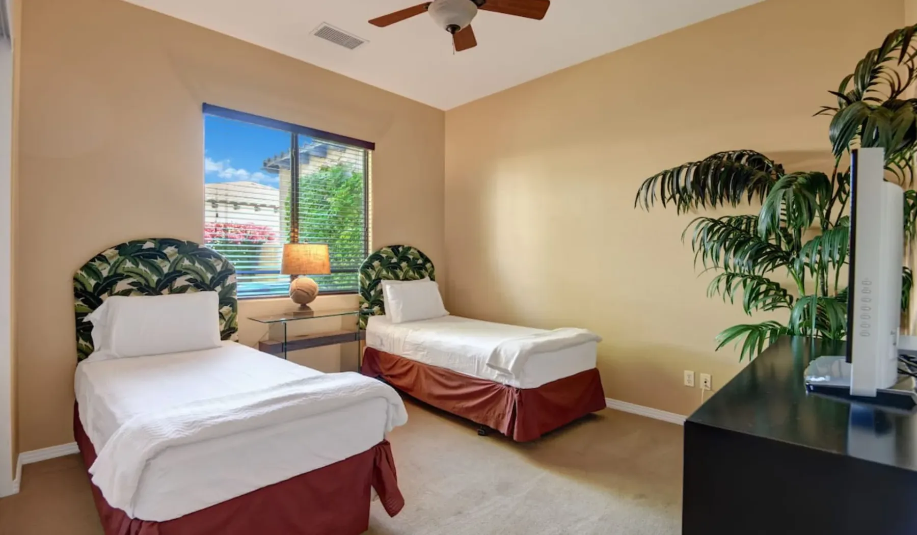 A bedroom with two beds beside a window and a leafy plant.