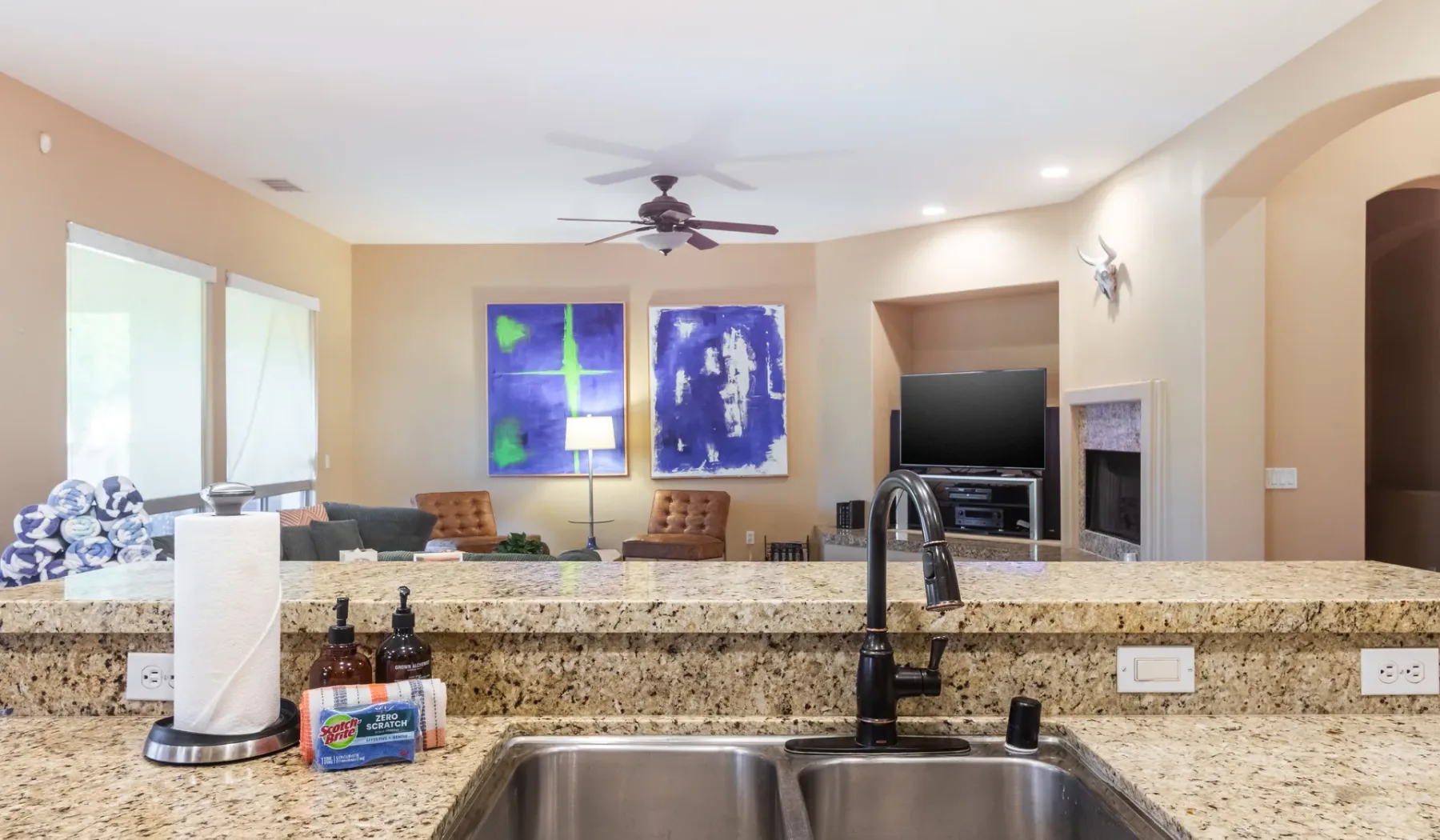 A living room with seating and a television is visible beyond the kitchen counter.