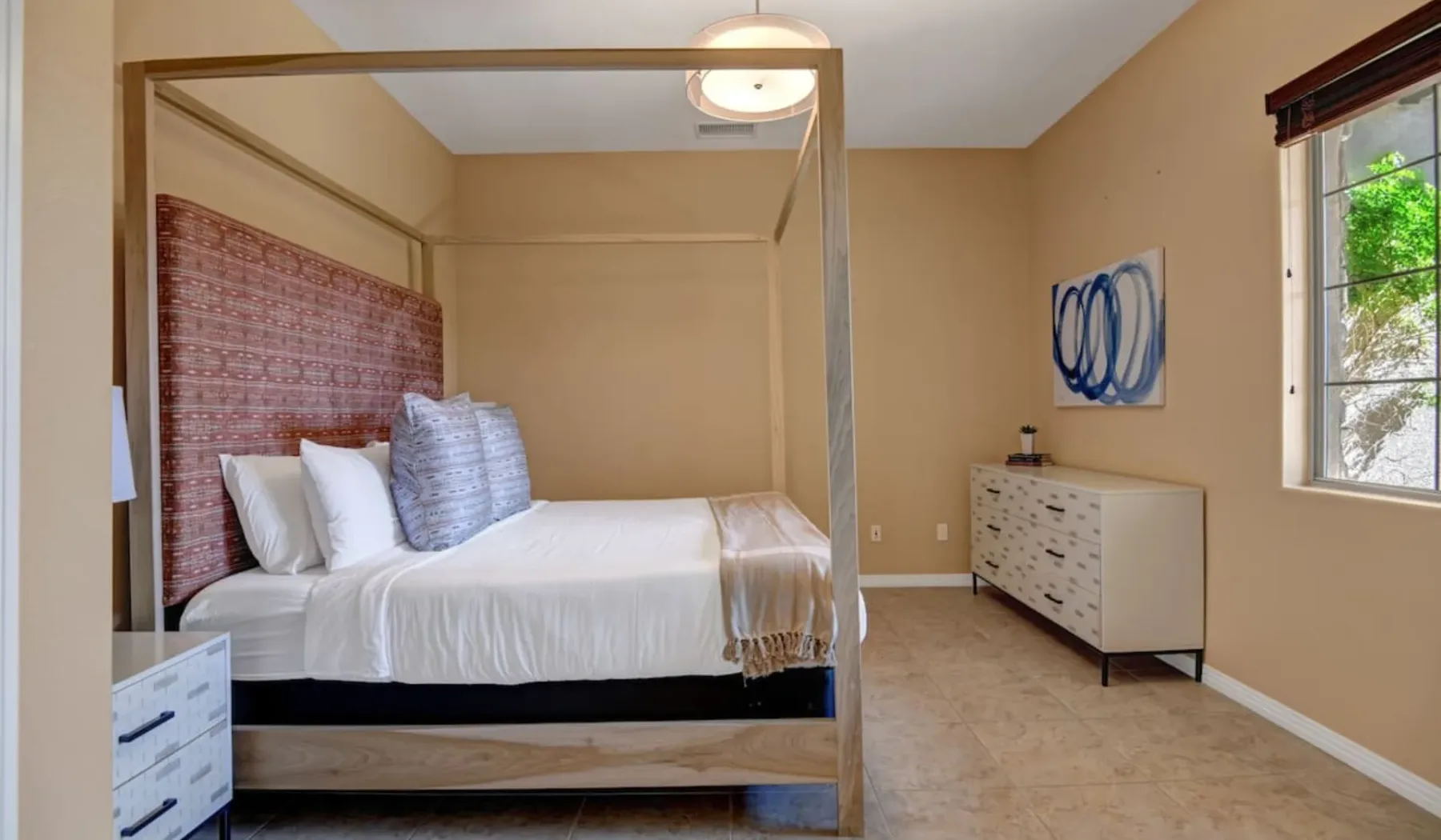 A bedroom with a canopy bed, a dresser, and a window.
