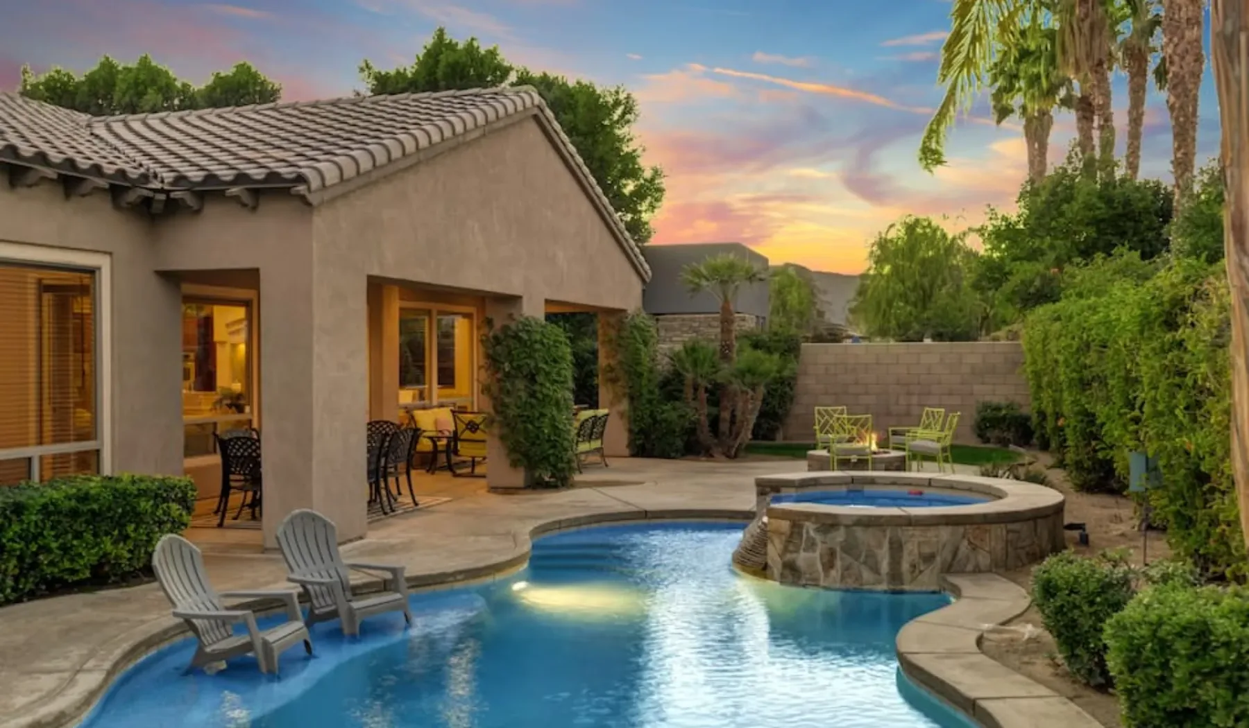 A backyard pool and raised spa sit beside a patio at sunset.