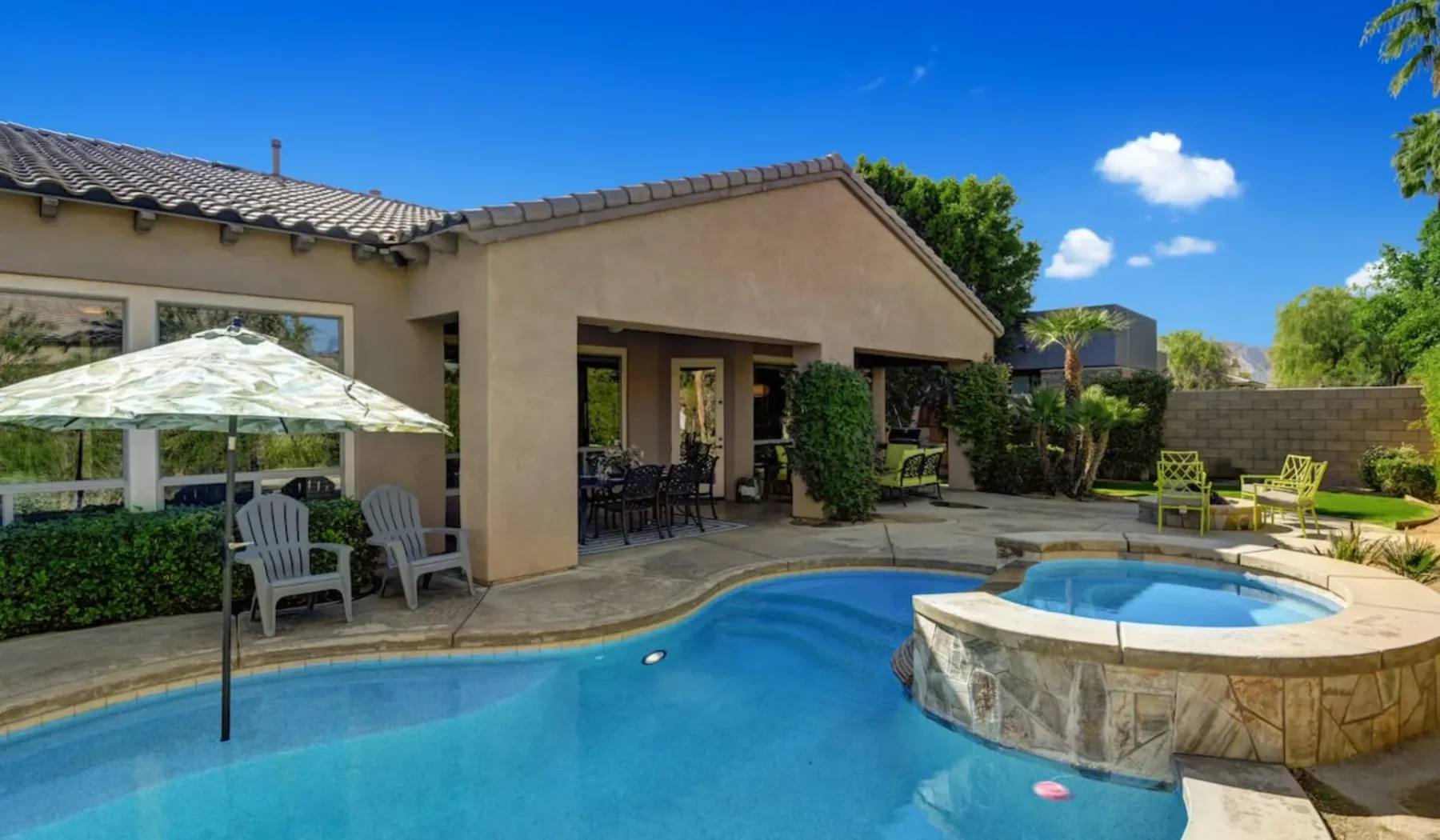 A swimming pool and raised circular spa sit beside a shaded patio.