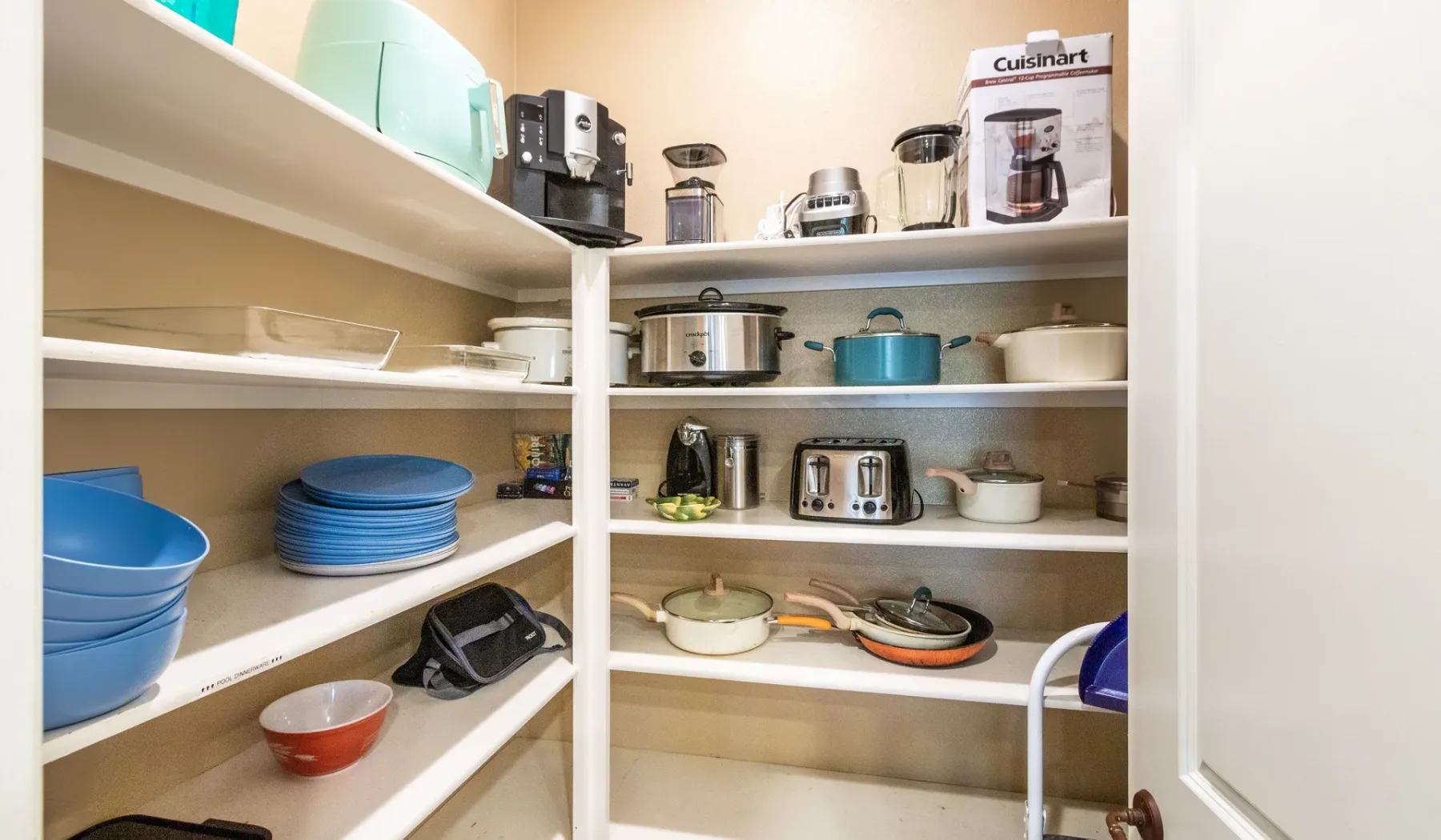 A pantry with open shelves holding kitchen appliances, cookware, and dishes.