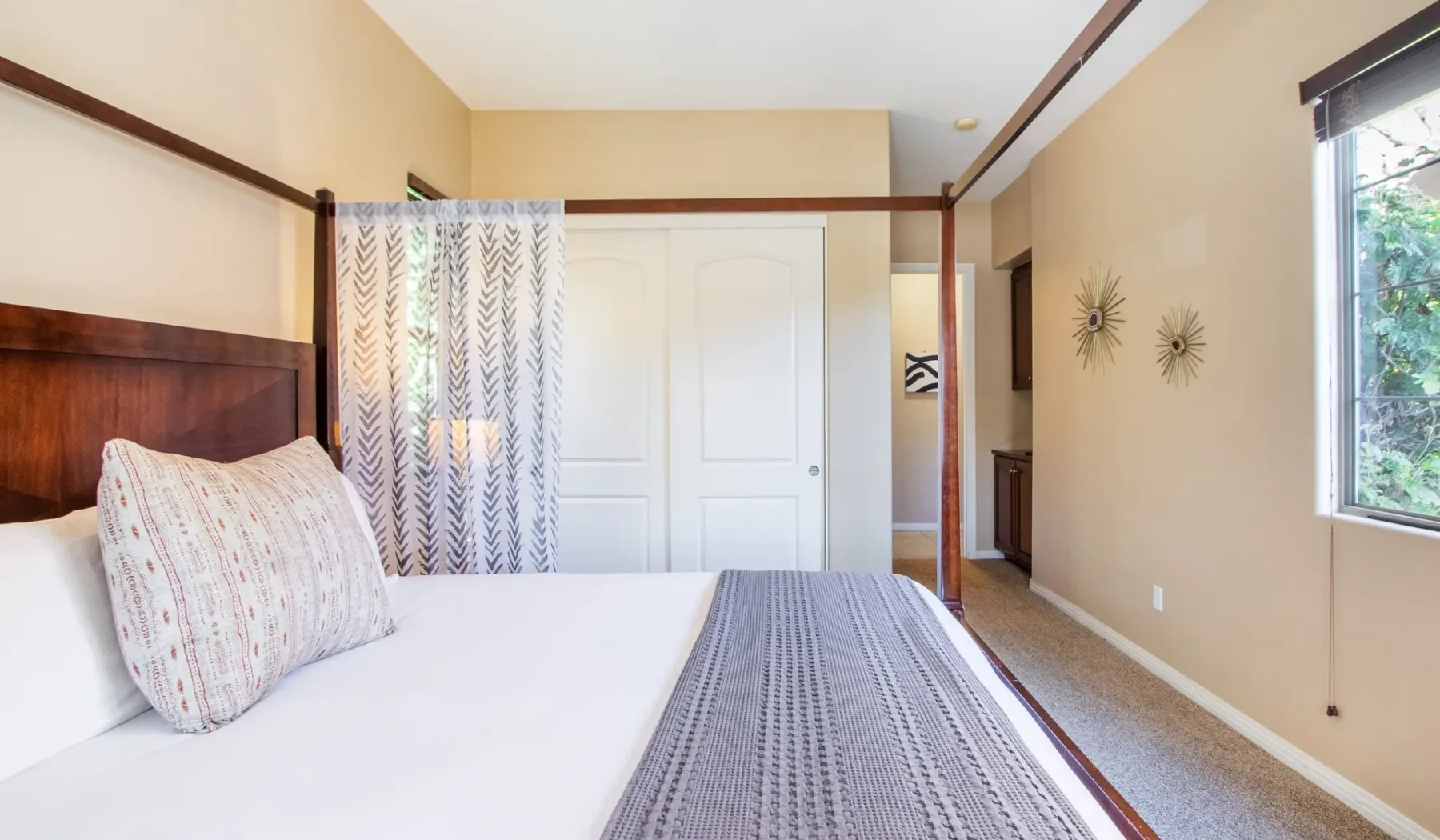 A bedroom with a neatly made bed, patterned curtain, and window.
