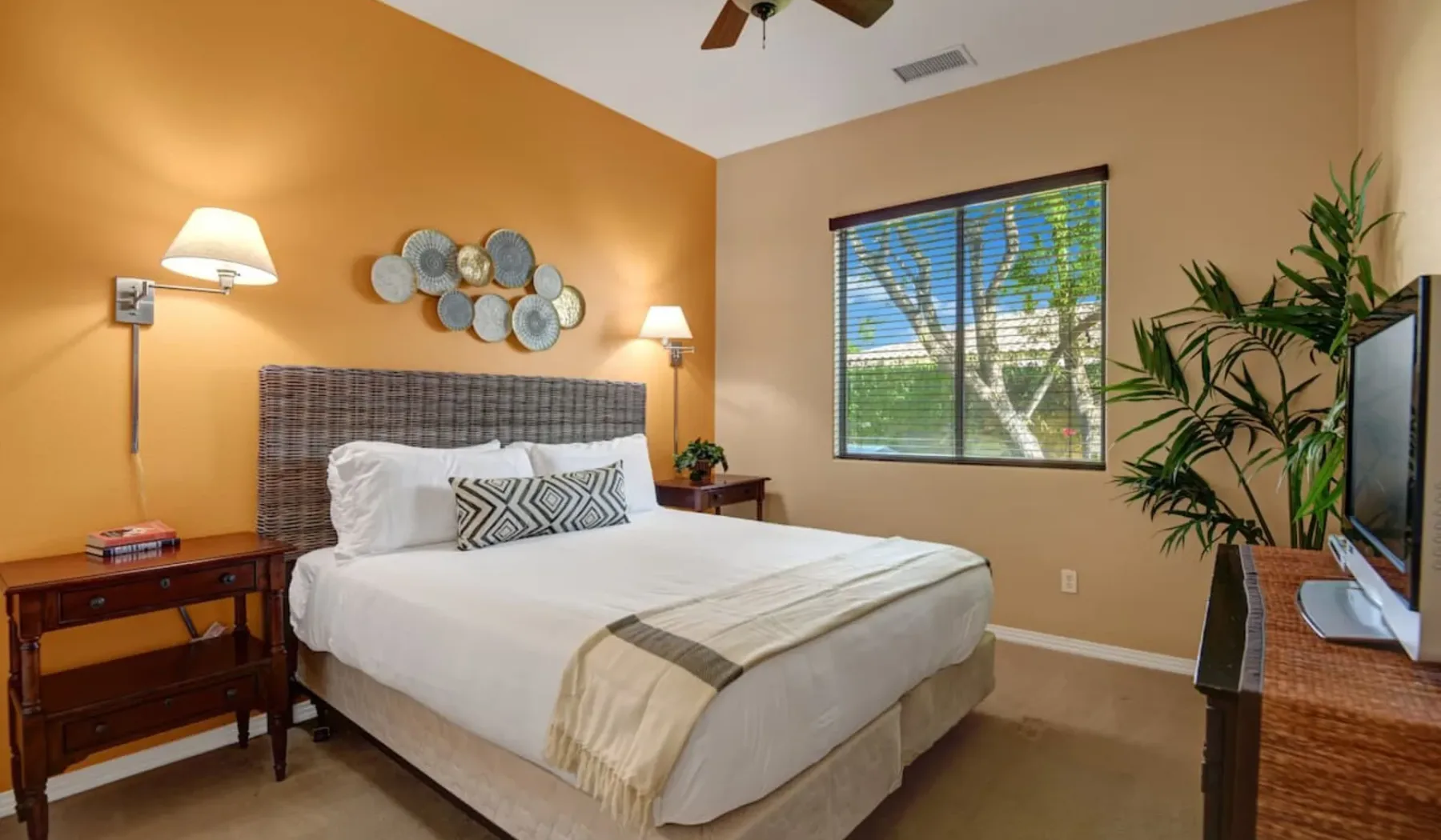 A bedroom with a neatly made bed, bedside tables, and a window with blinds.
