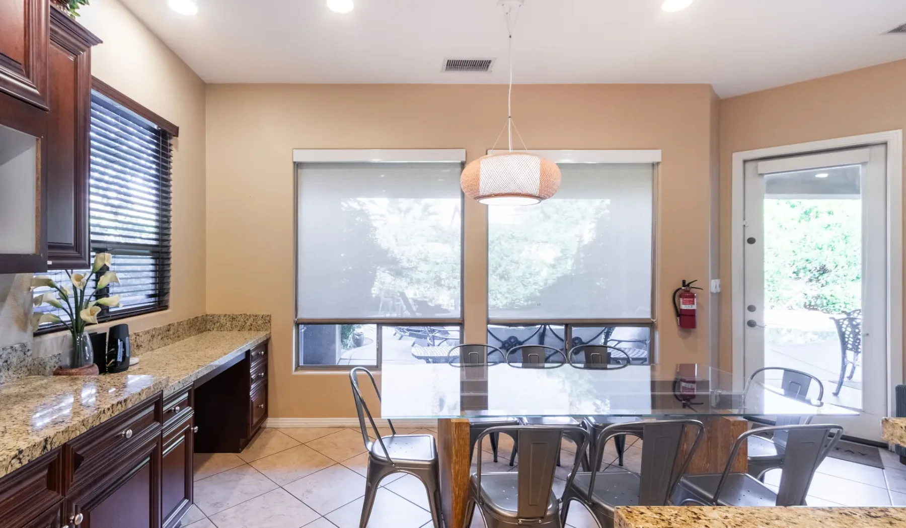 A dining area with a glass table and windows overlooking an outdoor patio.