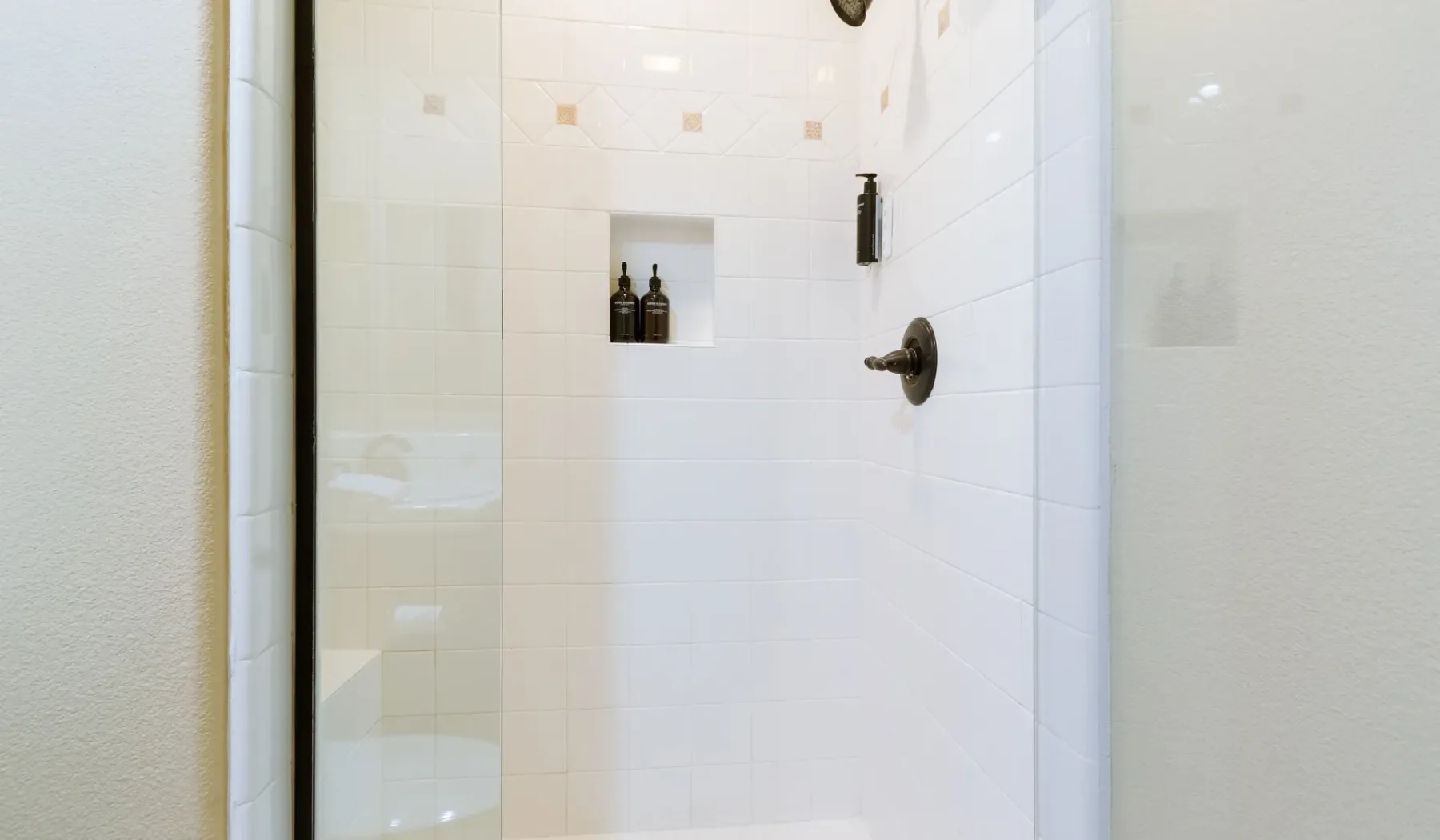 A tiled shower with a recessed shelf and wall-mounted fixtures.