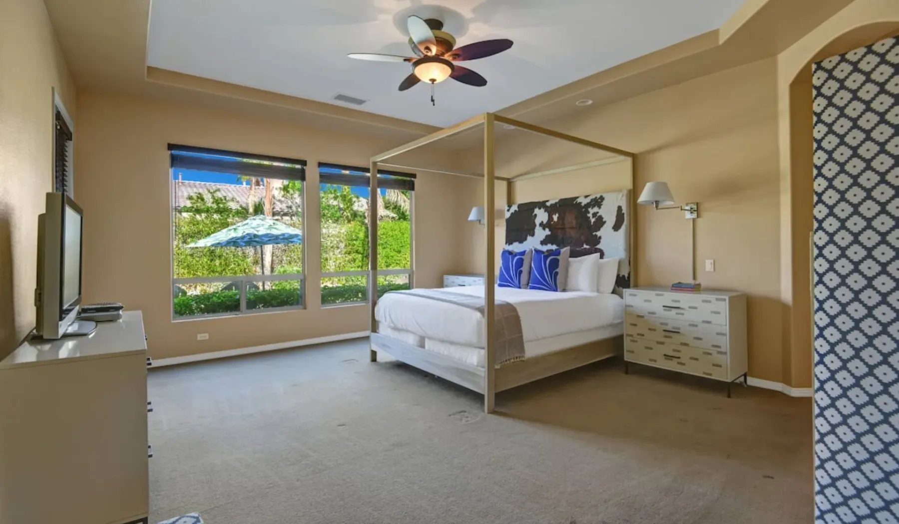 A bedroom with a canopy bed beside large windows.