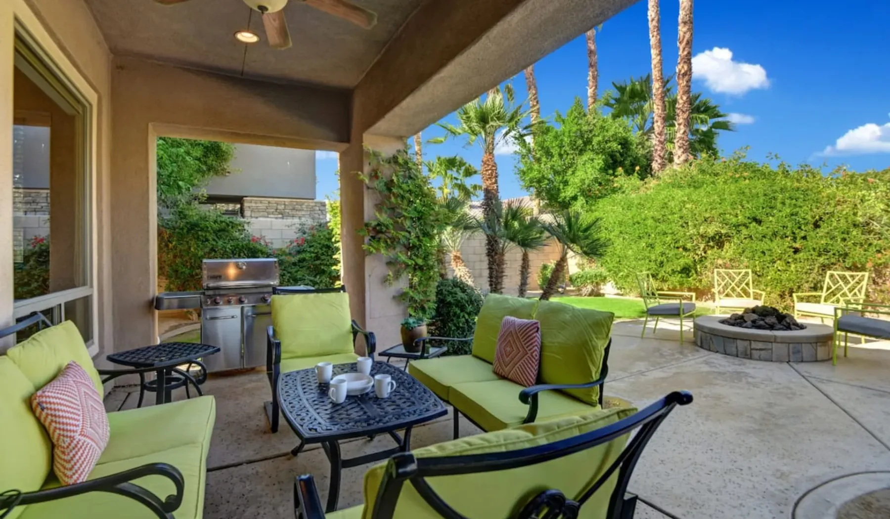 A covered outdoor patio with cushioned seating, a dining table, and a grill.