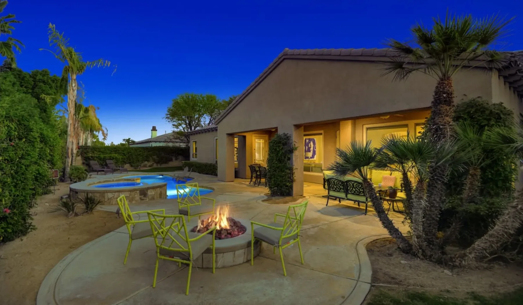 An outdoor patio with a small pool, seating, and a fire pit beside a house.