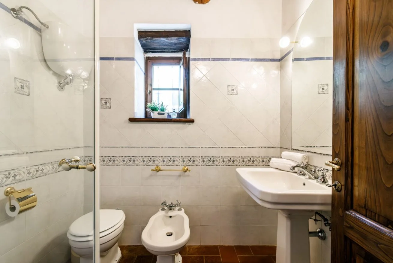 A tiled bathroom with a shower, sink, toilet, and window.