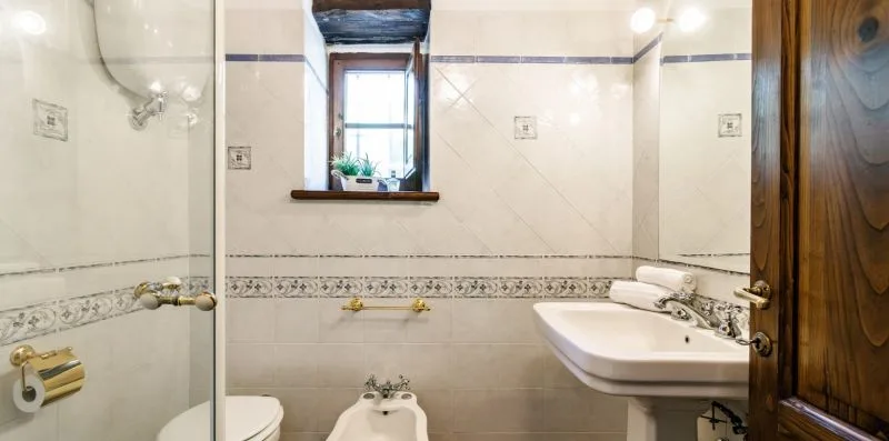 A tiled bathroom with a sink, toilet, and small window.