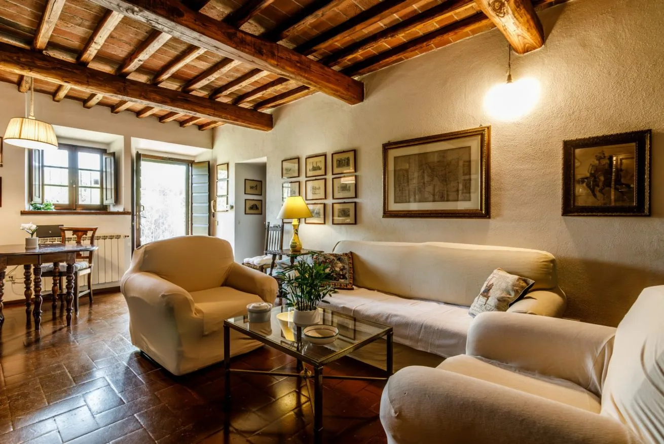 A living room with upholstered seating, framed artwork, and exposed ceiling beams.