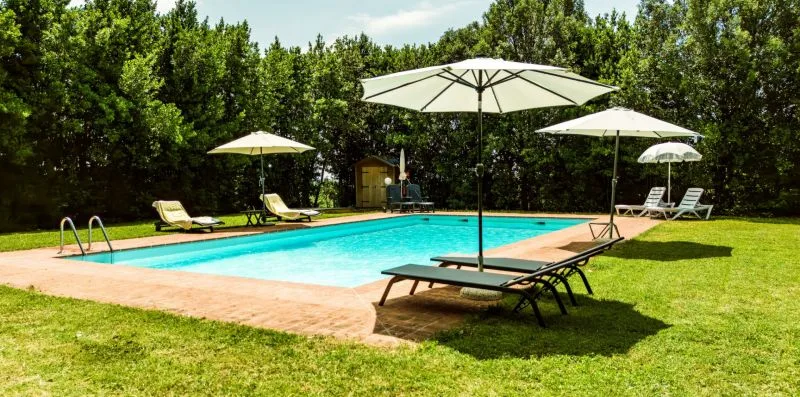An outdoor swimming pool with loungers and umbrellas on a grassy lawn.