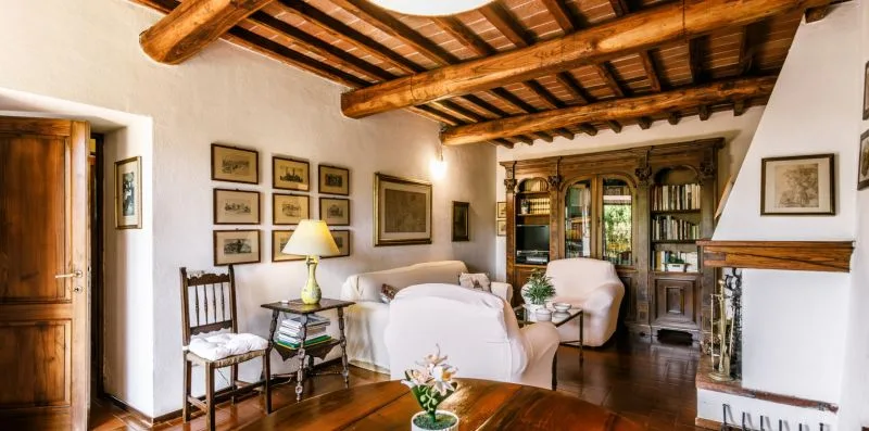 A living room with pale seating, a wooden bookcase, and exposed ceiling beams.