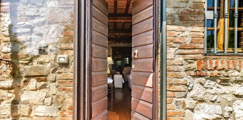 An open wooden doorway in a stone wall reveals a room with a bed.