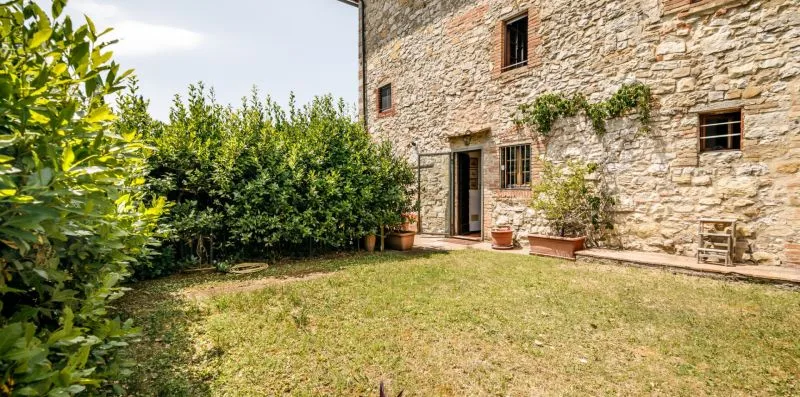 A grassy courtyard beside a stone building, with shrubs along the edge.