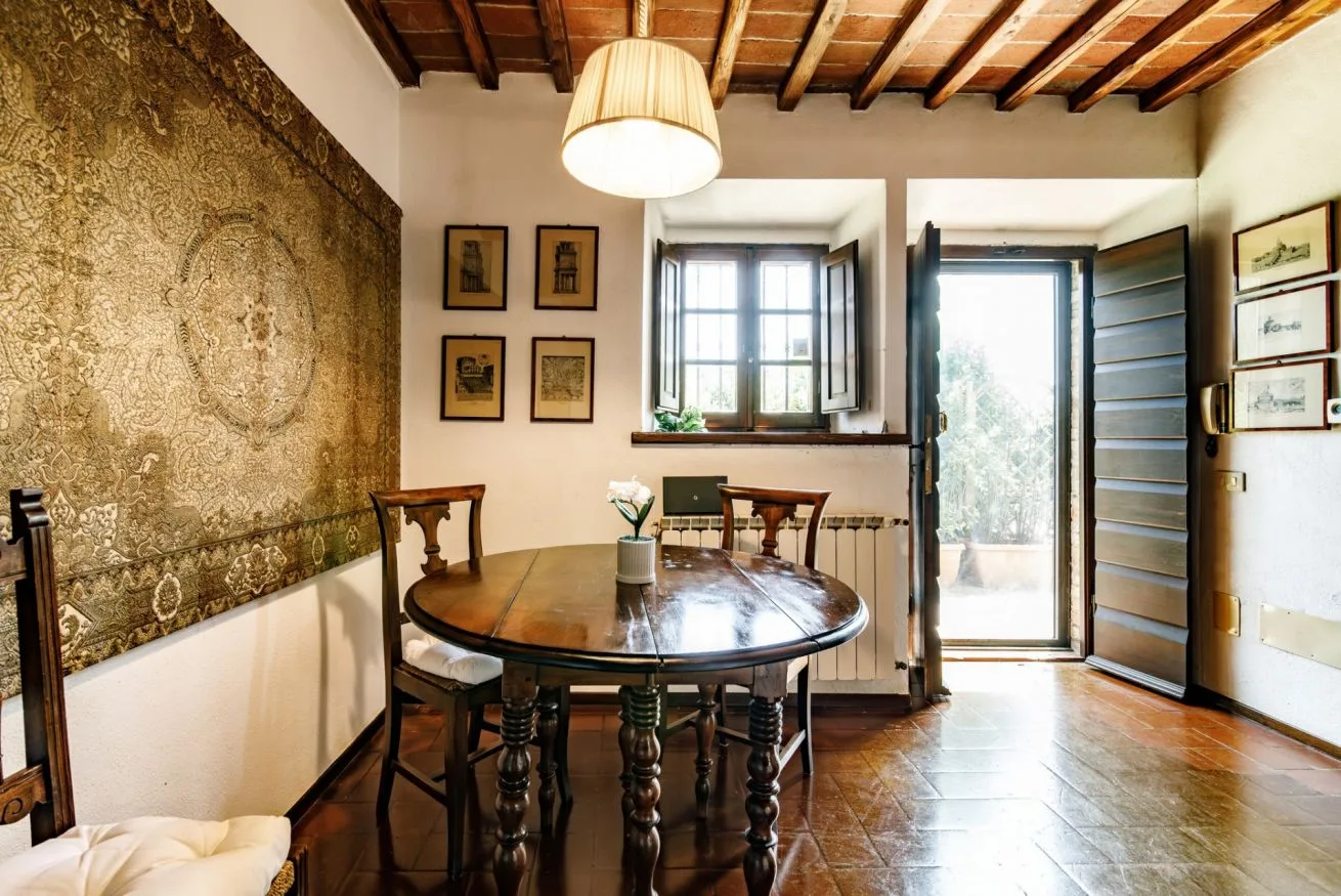 A dining area with a round table beneath exposed wooden ceiling beams.