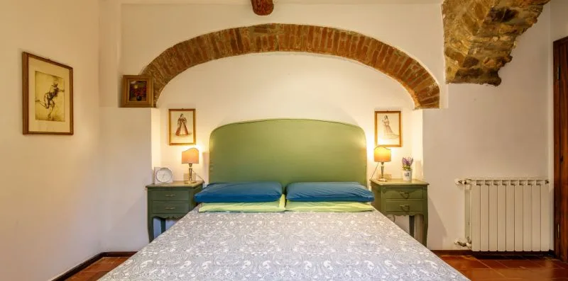 A bedroom with a bed, bedside tables, and an exposed brick arch.