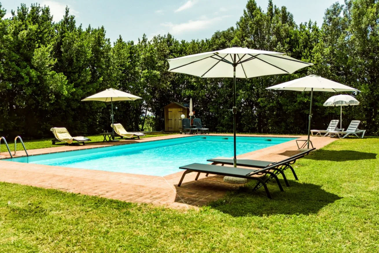 A swimming pool is surrounded by a grassy lawn, loungers, and umbrellas.