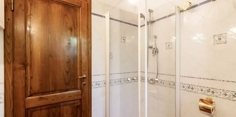 A tiled bathroom with a glass shower and a wooden door.