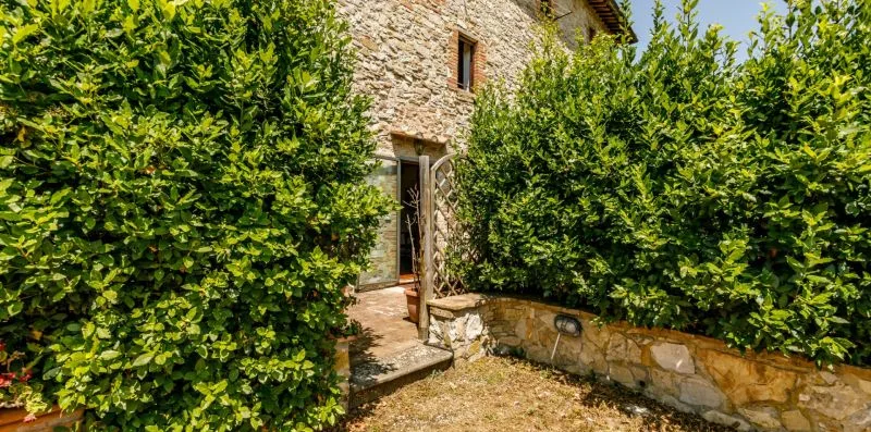 A stone building entrance is partly screened by dense green hedges.