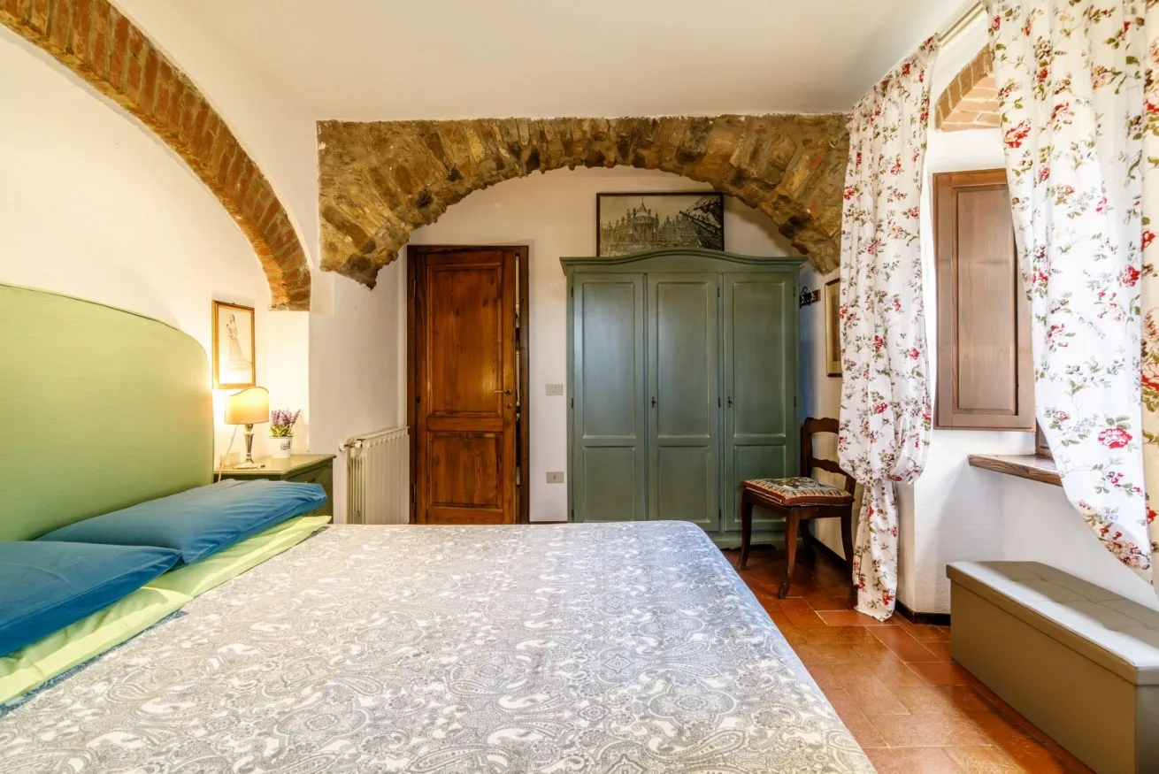 A bedroom with a patterned bedspread, a green wardrobe, and floral curtains.