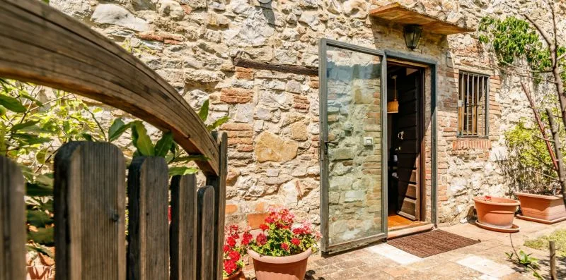 A stone building entrance opens onto a small patio with potted flowers.