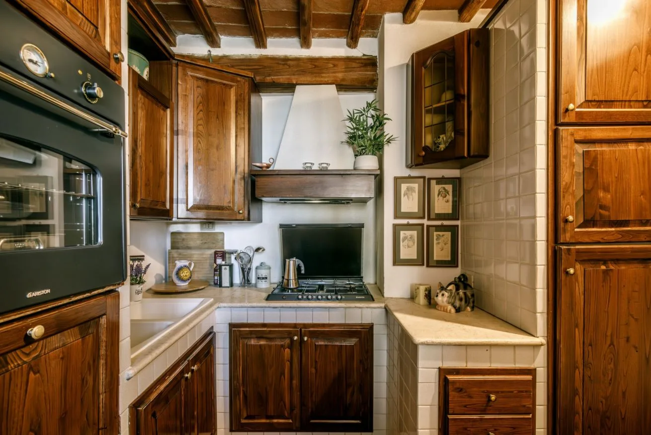 A kitchen with wooden cabinets, a cooktop, and exposed ceiling beams.