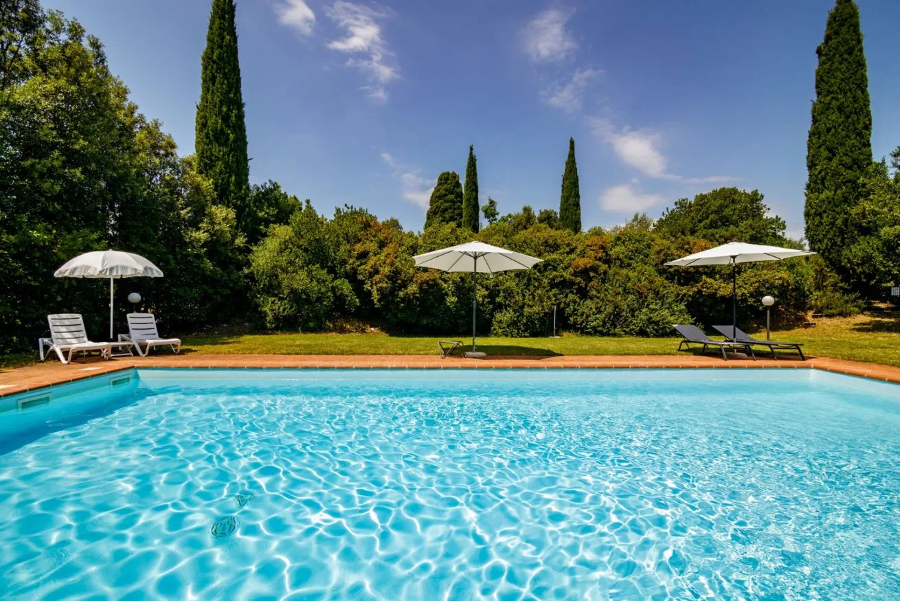 An outdoor swimming pool is surrounded by greenery and shaded seating.