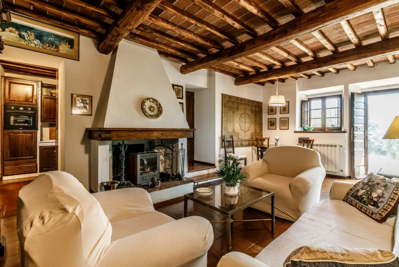A living room with cream seating around a fireplace beneath exposed wooden ceiling beams.
