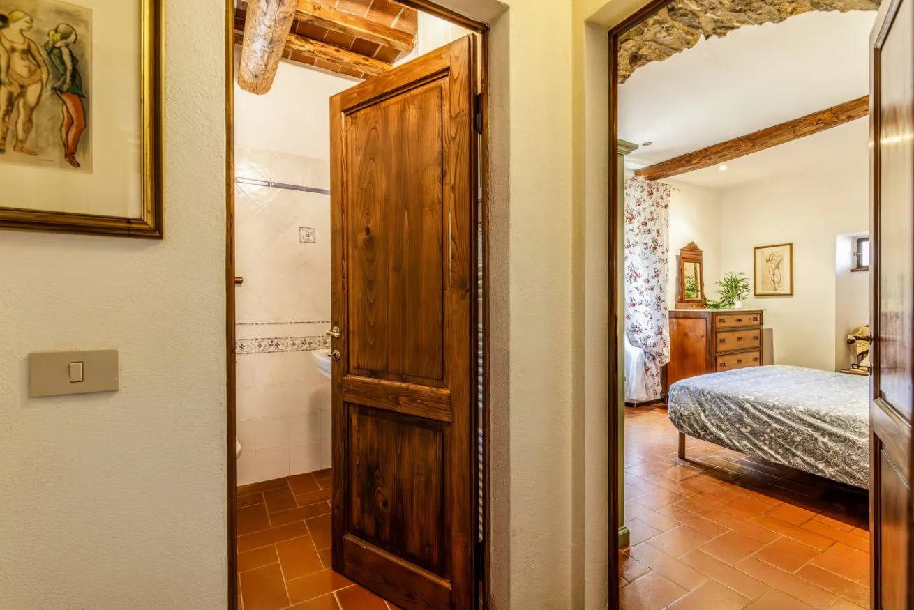 A tiled hallway opens through a wooden doorway into a bedroom.