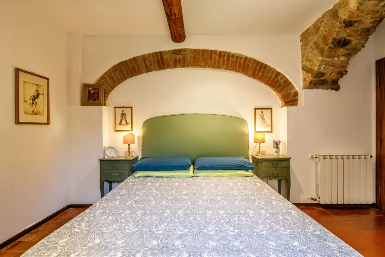 A bedroom with a bed beneath a brick arch and a green headboard.