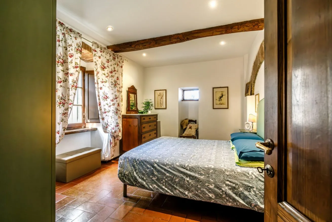 A bedroom with a bed, floral curtains, and a wooden beam across the ceiling.