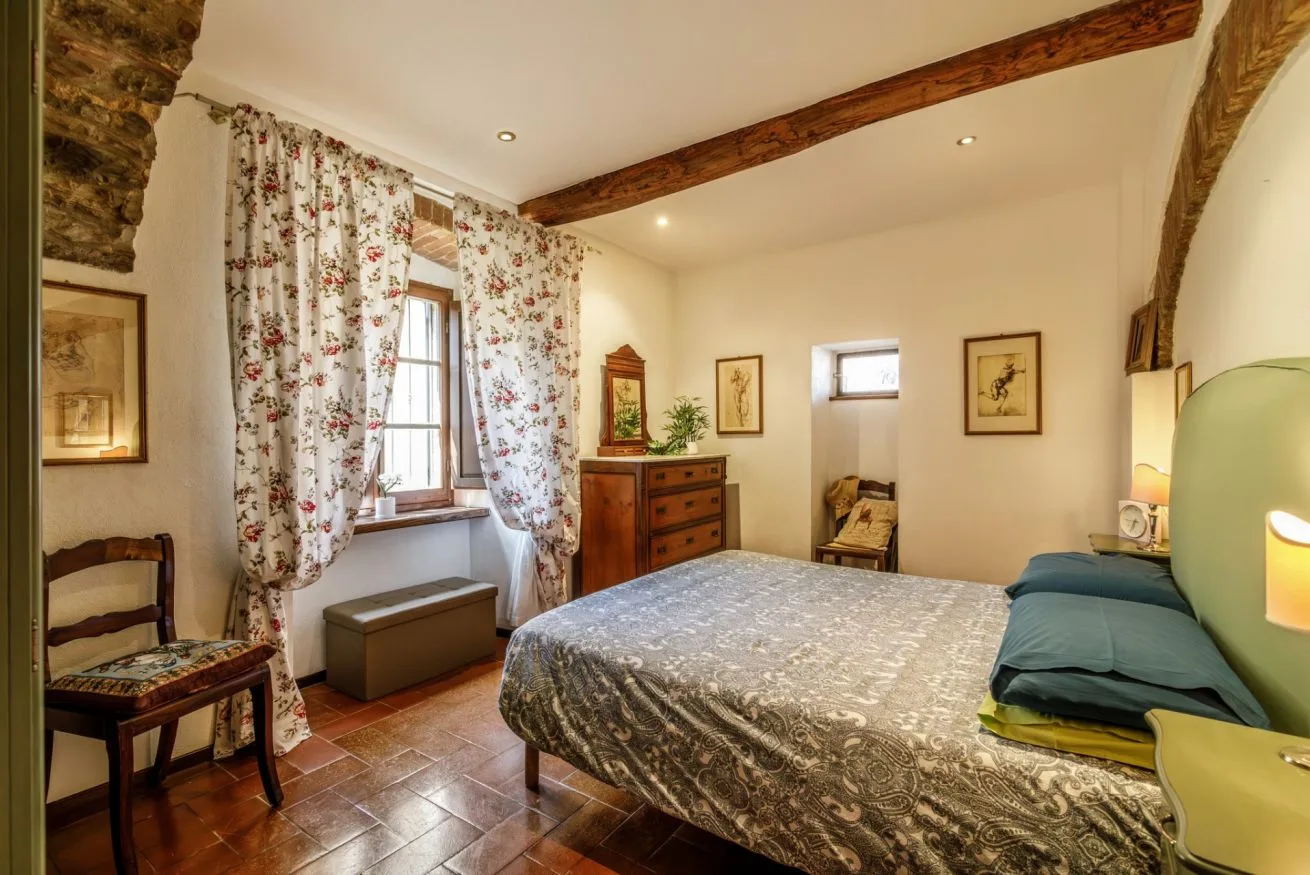 A bedroom with a large bed, floral curtains, and a wooden dresser.