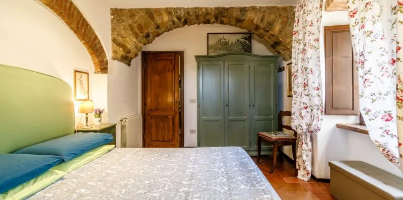 A bedroom with a large bed, green wardrobe, and floral curtains.
