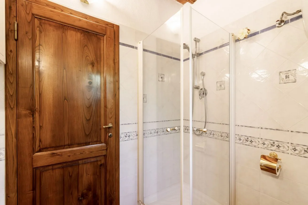 A tiled bathroom with a glass shower and a wooden door.
