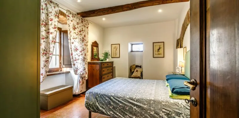 A bedroom with a bed, wooden dresser, and floral curtains by the window.