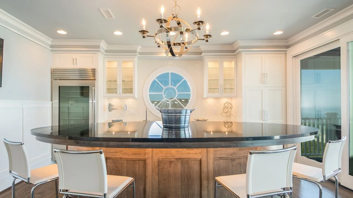A bright kitchen with a curved island, bar seating, and white cabinetry.