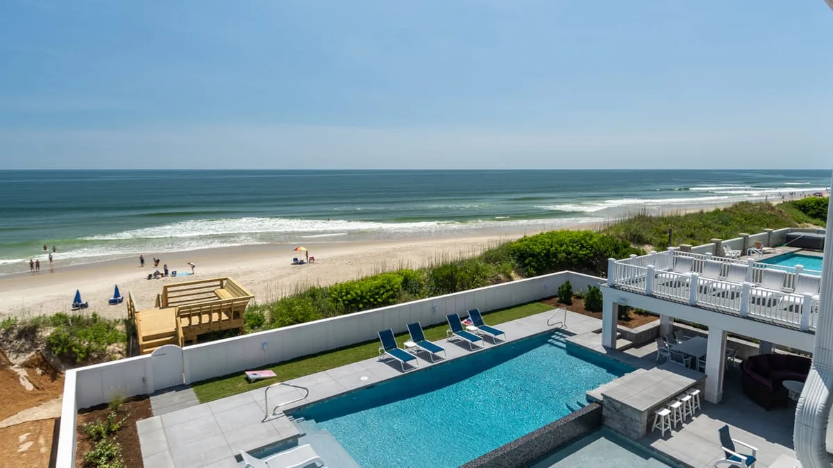A seaside pool area overlooks a sandy beach and the ocean.
