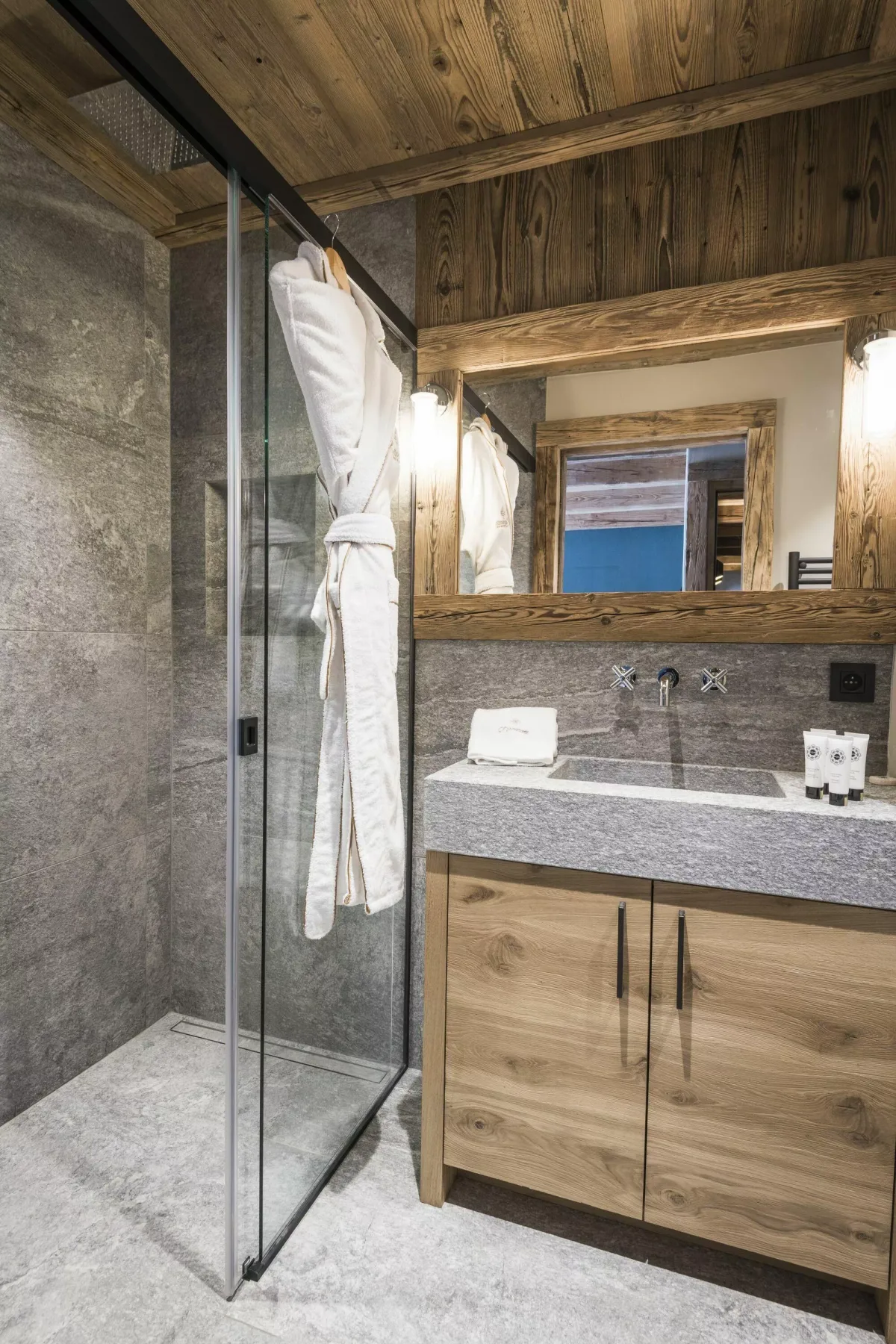 Un baño con una ducha de vidrio junto a un tocador de madera y un espejo.