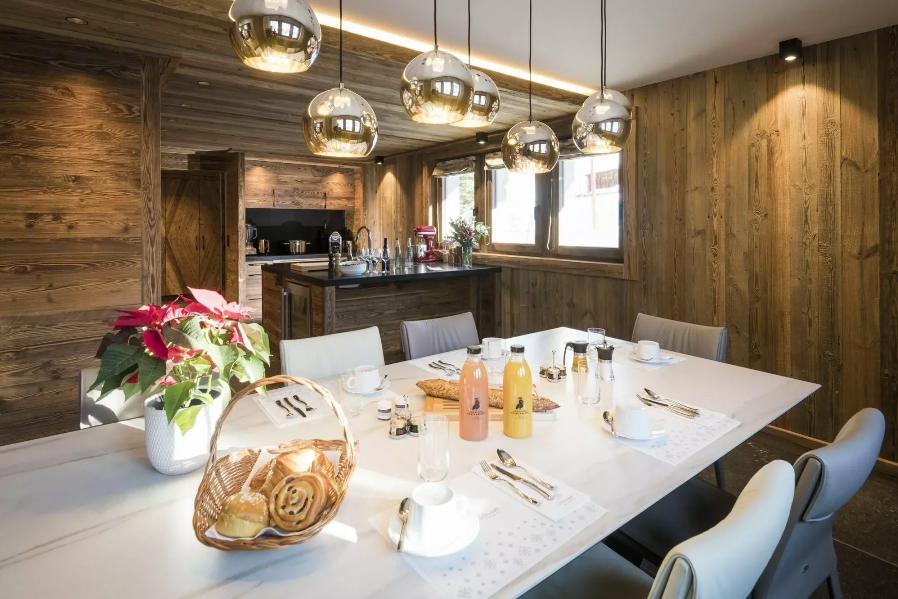 Un comedor con la mesa puesta, lámparas colgantes y una cocina revestida de madera.