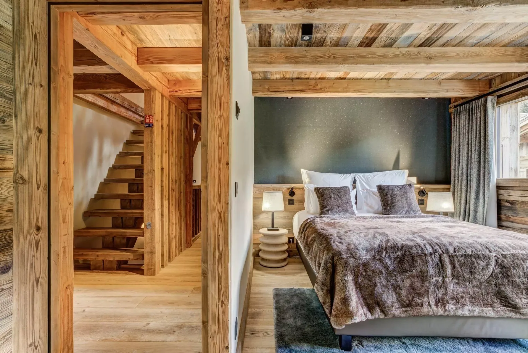 Un dormitorio con una cama junto a una ventana con cortinas y una escalera de madera.